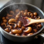 A simmering saucepan of red wine and mushroom jus reducing on a stovetop, with steam rising and rich aromas filling the kitchen.