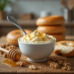 A joyful woman smiling while enjoying a bagel topped with honey walnut cream cheese, highlighting the creamy and rich texture.