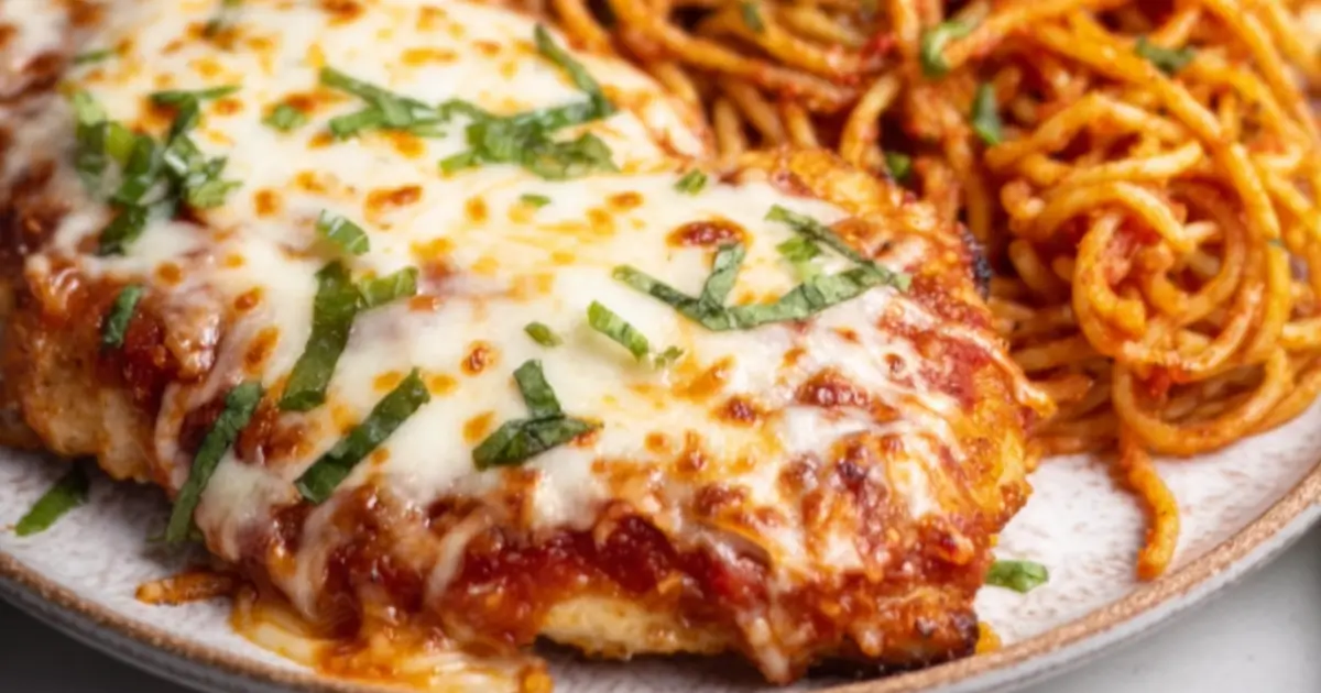 Baked chicken parmesan topped with melted mozzarella and fresh basil, served with spaghetti.