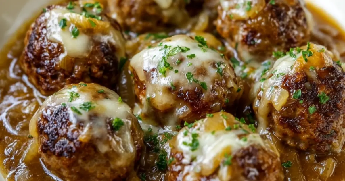 Skillet filled with French onion meatballs smothered in caramelized onion sauce and melted cheese, garnished with fresh herbs
