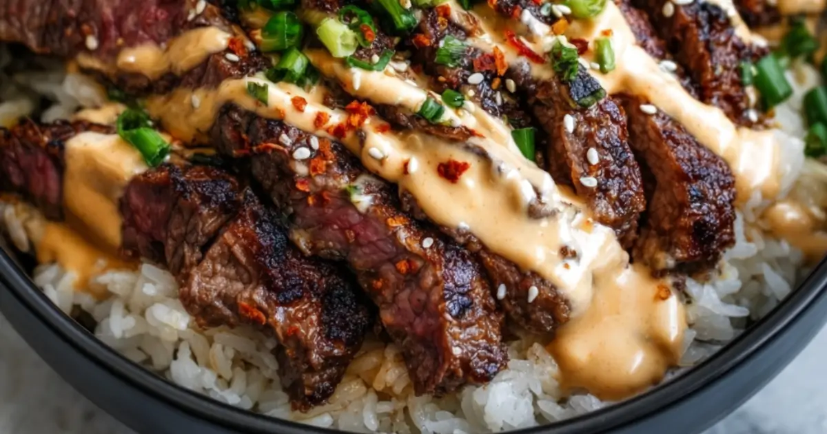 Korean BBQ steak rice bowl topped with spicy cream sauce, sesame seeds, and fresh green onions.