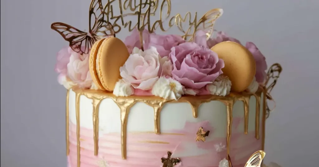 floral drip birthday cake with pink roses, gold accents, and macarons