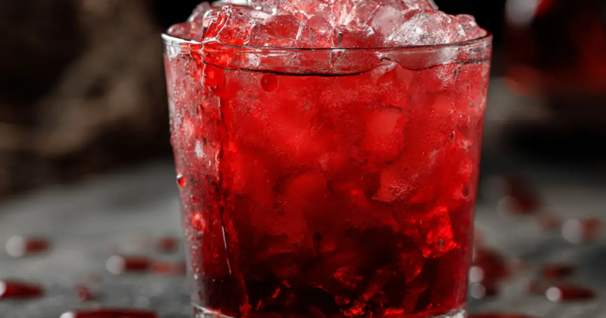 Chilling red cocktail over crushed ice in a glass, resembling blood, with a dark moody background
