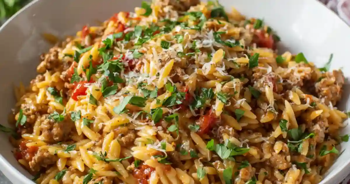 Bowl of creamy orzo pasta with sausage, cherry tomatoes, parmesan, and fresh parsley