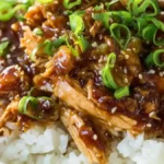 bowl of shredded crockpot teriyaki chicken over sticky white rice with sesame seeds and green onions