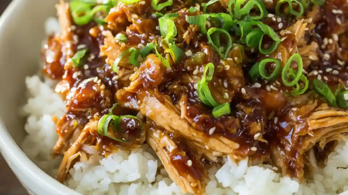 bowl of shredded crockpot teriyaki chicken over sticky white rice with sesame seeds and green onions