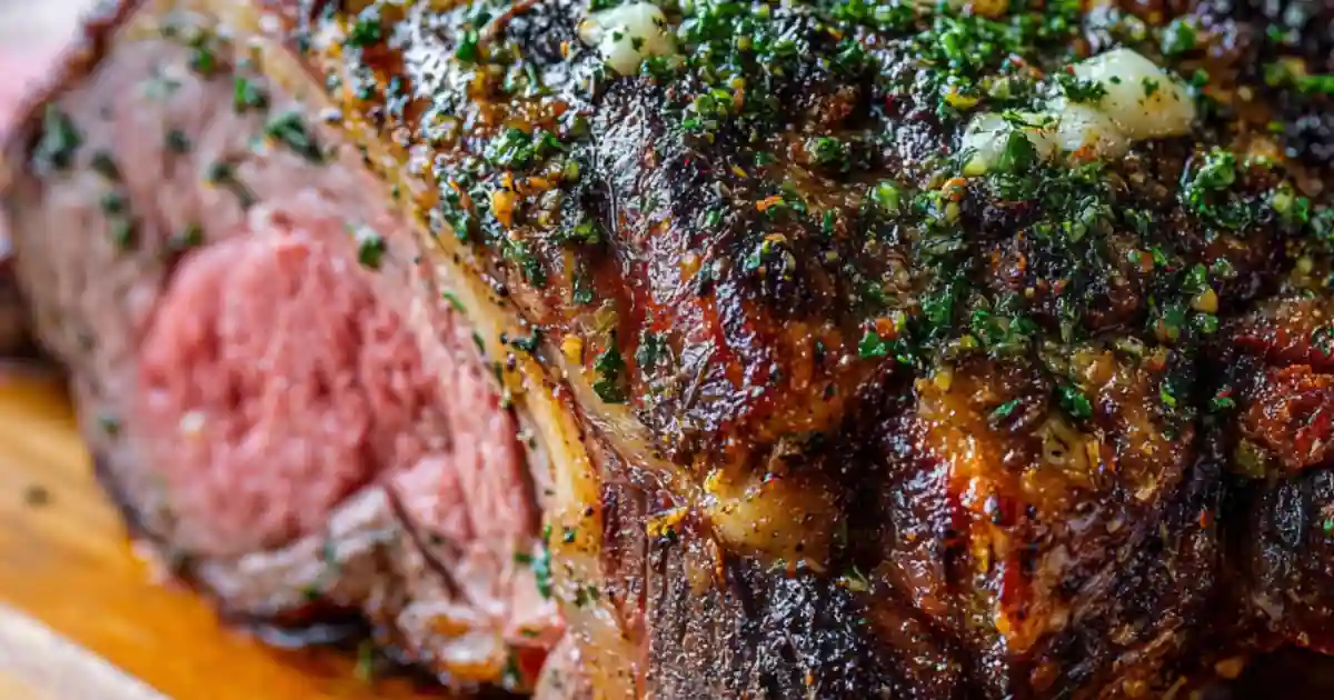 Close-up of roasted garlic herb prime rib with crispy crust and juicy pink center, topped with garlic and herbs.