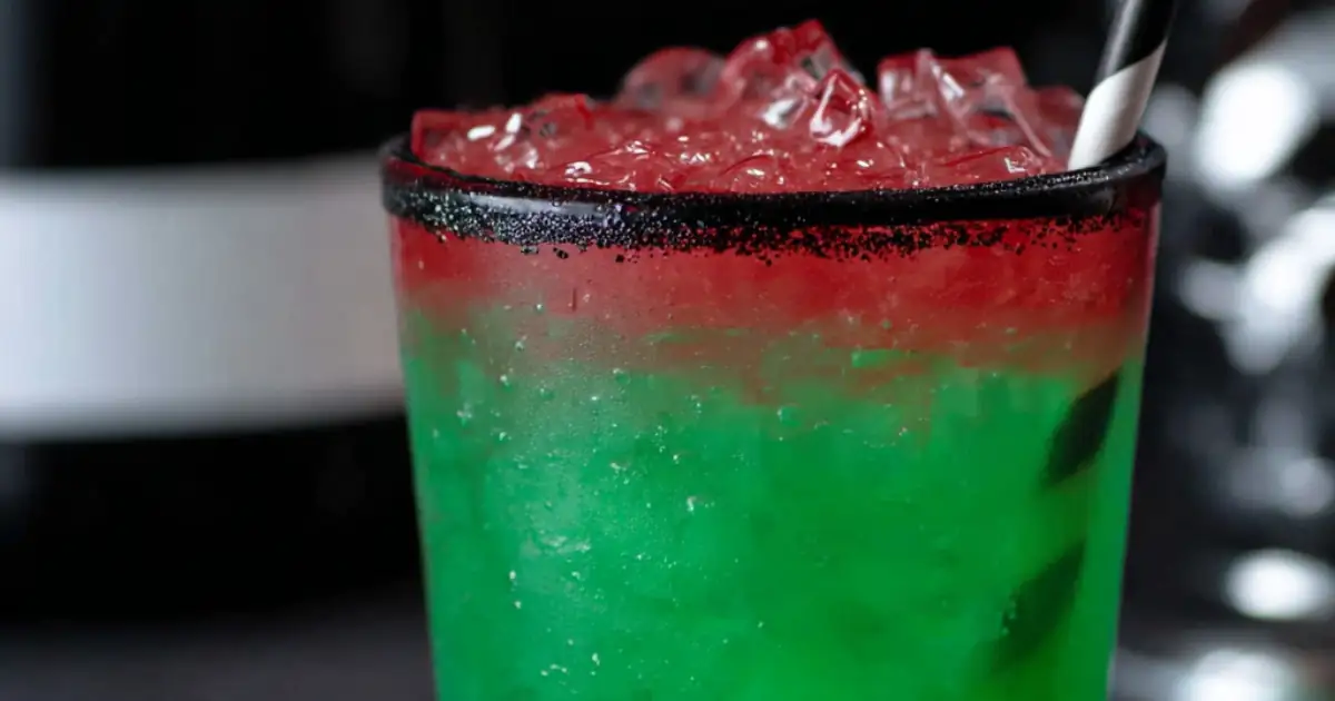 Layered green and red Halloween cocktail with black sugar rim and straw in a glass