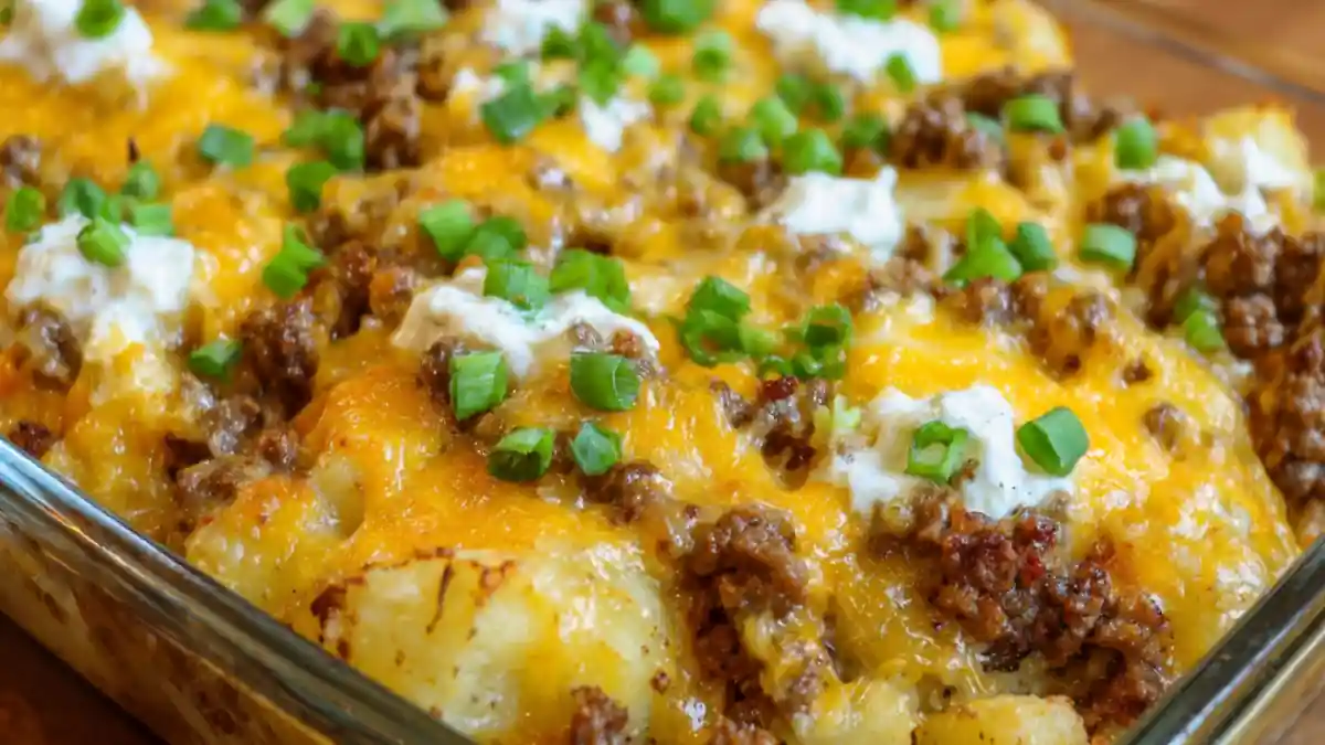 loaded beef and potato casserole topped with cheddar, sour cream, and green onions in glass dish