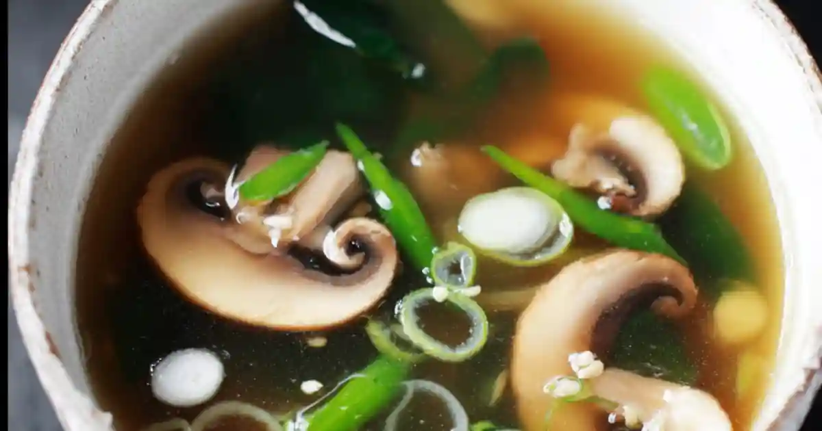 miso soup with mushrooms, scallions, and green vegetables in a ceramic bowl