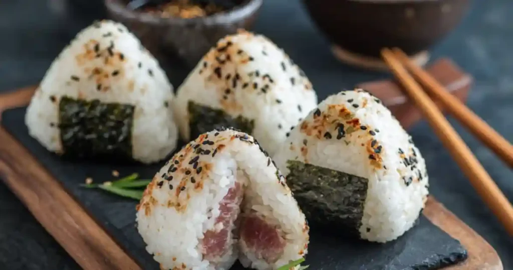 Japanese onigiri rice balls with sesame seeds, seaweed, and tuna filling on a slate board