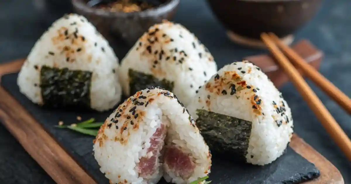 Japanese onigiri rice balls with sesame seeds, seaweed, and tuna filling on a slate board