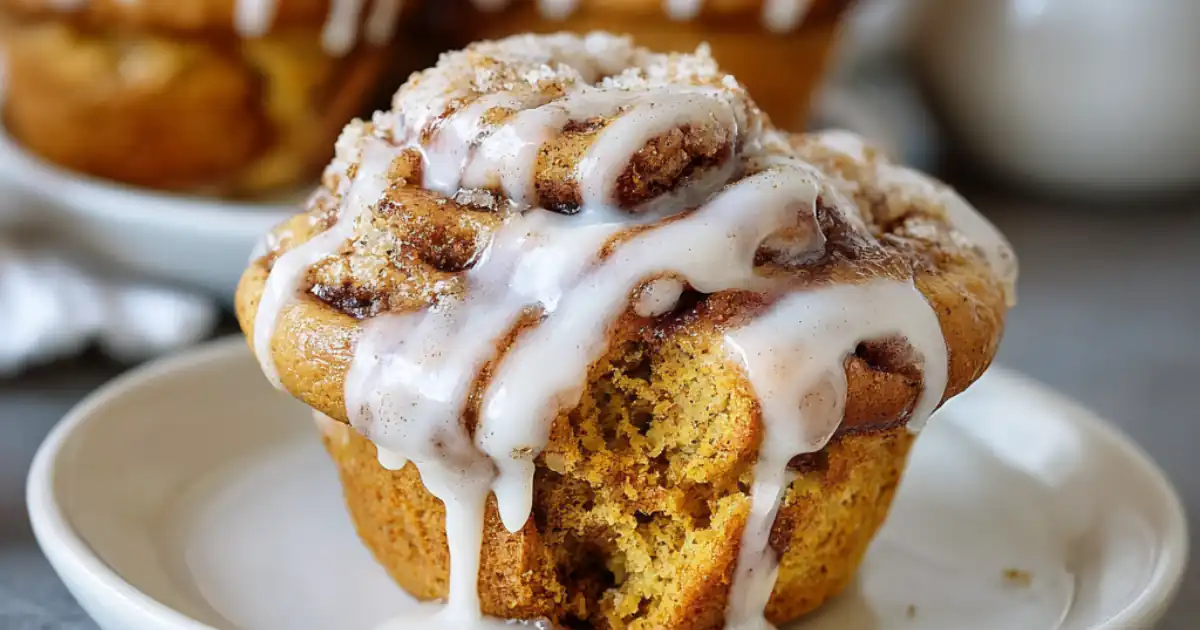 Pumpkin cinnamon roll muffin topped with vanilla icing drizzle on a white plate