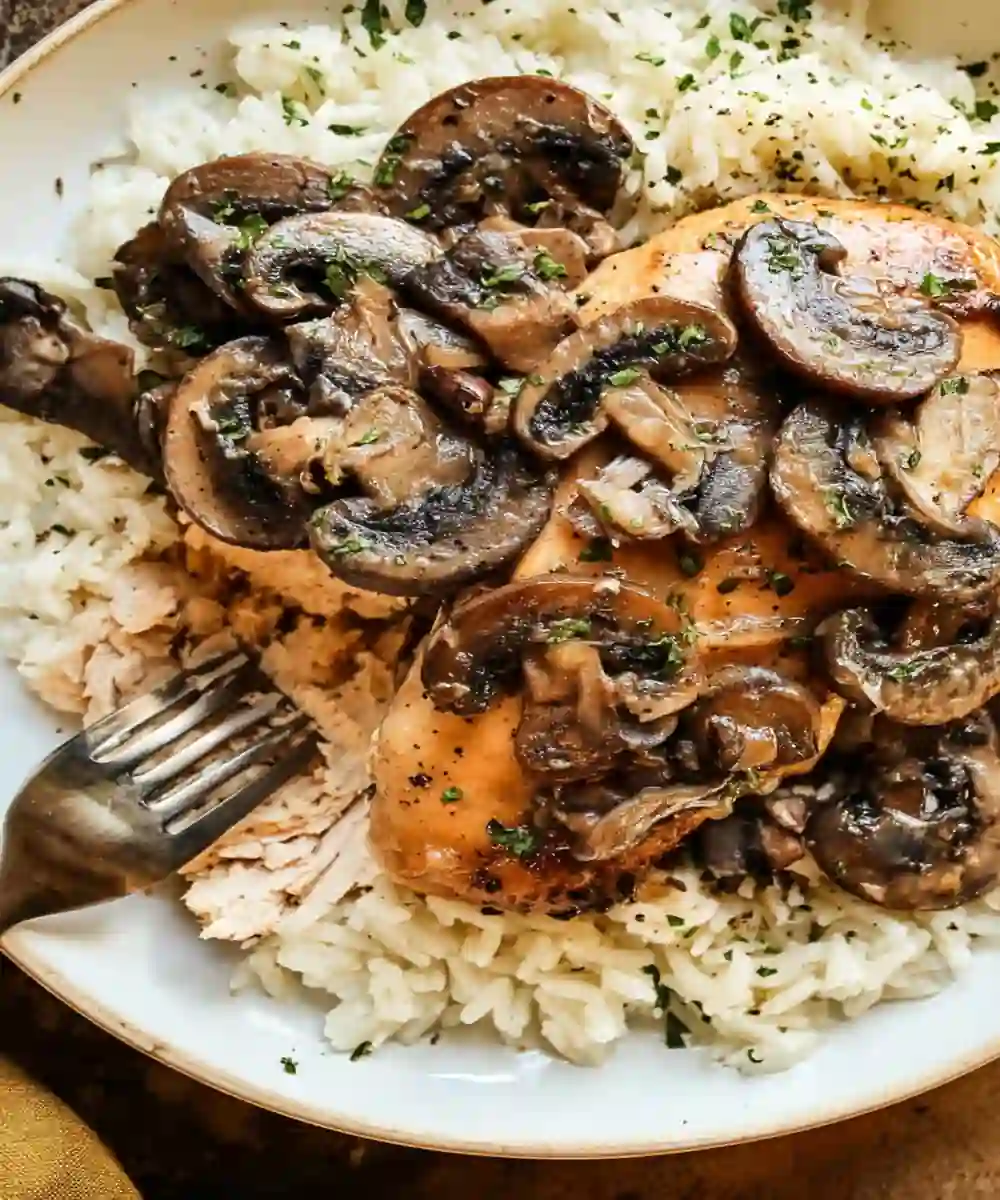 Slow cooker chicken marsala topped with sautéed mushrooms served over fluffy white rice in a white plate