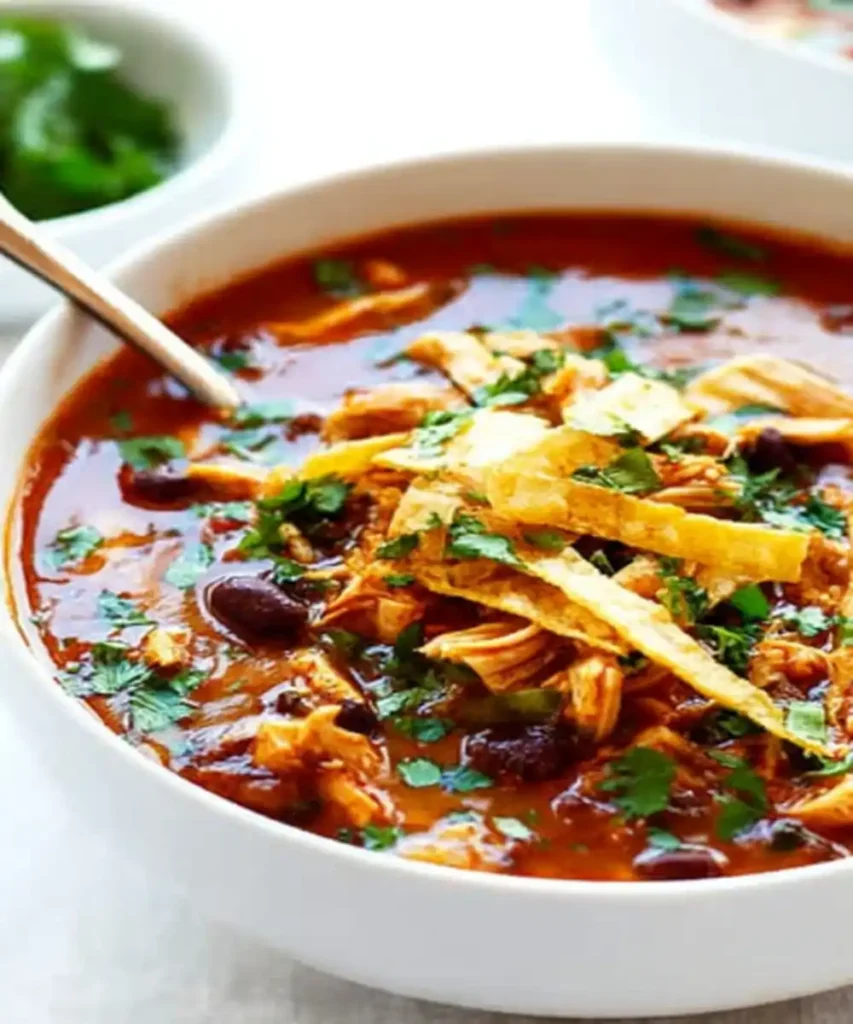 Bowl of chicken tortilla soup with shredded chicken, black beans, tortilla strips, and fresh cilantro