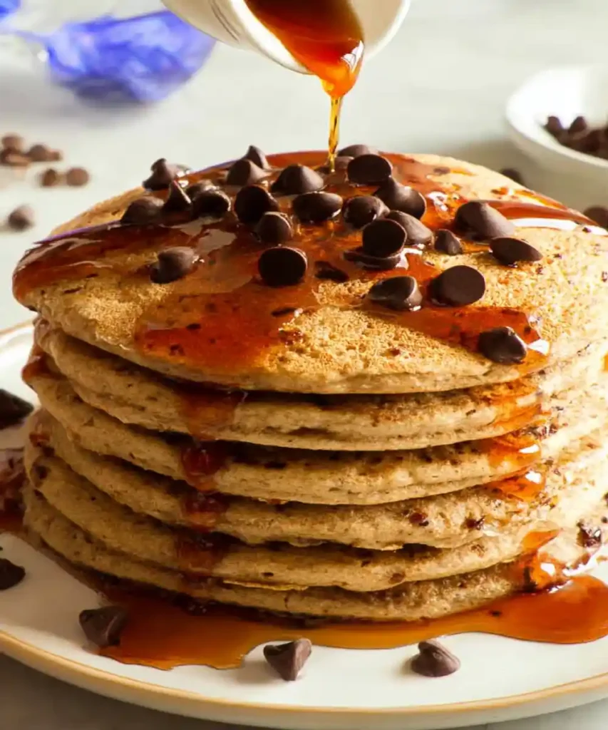 Stack of chocolate chip pancakes topped with syrup and chocolate chips being poured with maple syrup