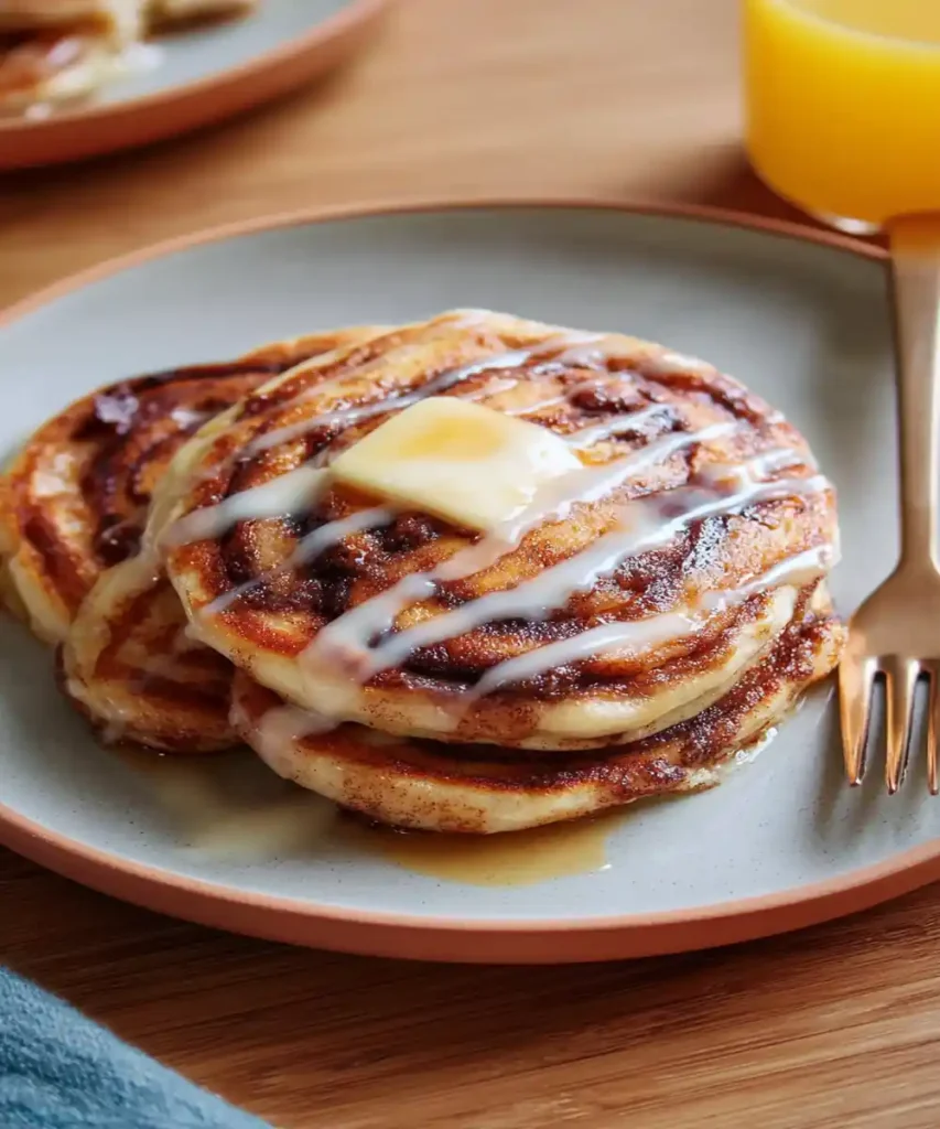 Stack of cinnamon swirl pancakes topped with melted butter and icing drizzle on a plate