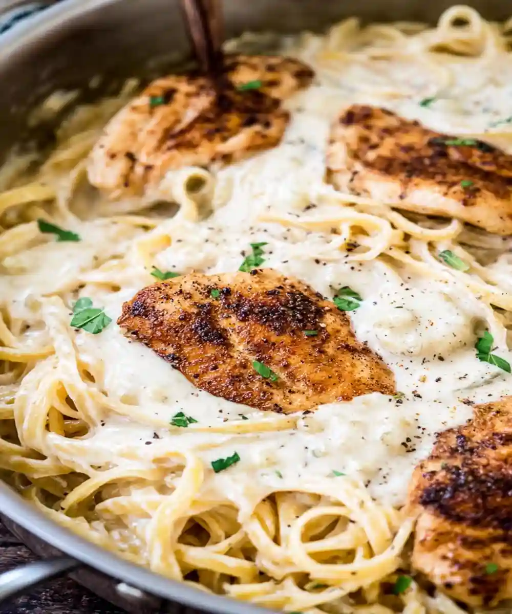 Creamy chicken alfredo pasta with grilled chicken breasts and fettuccine in a skillet