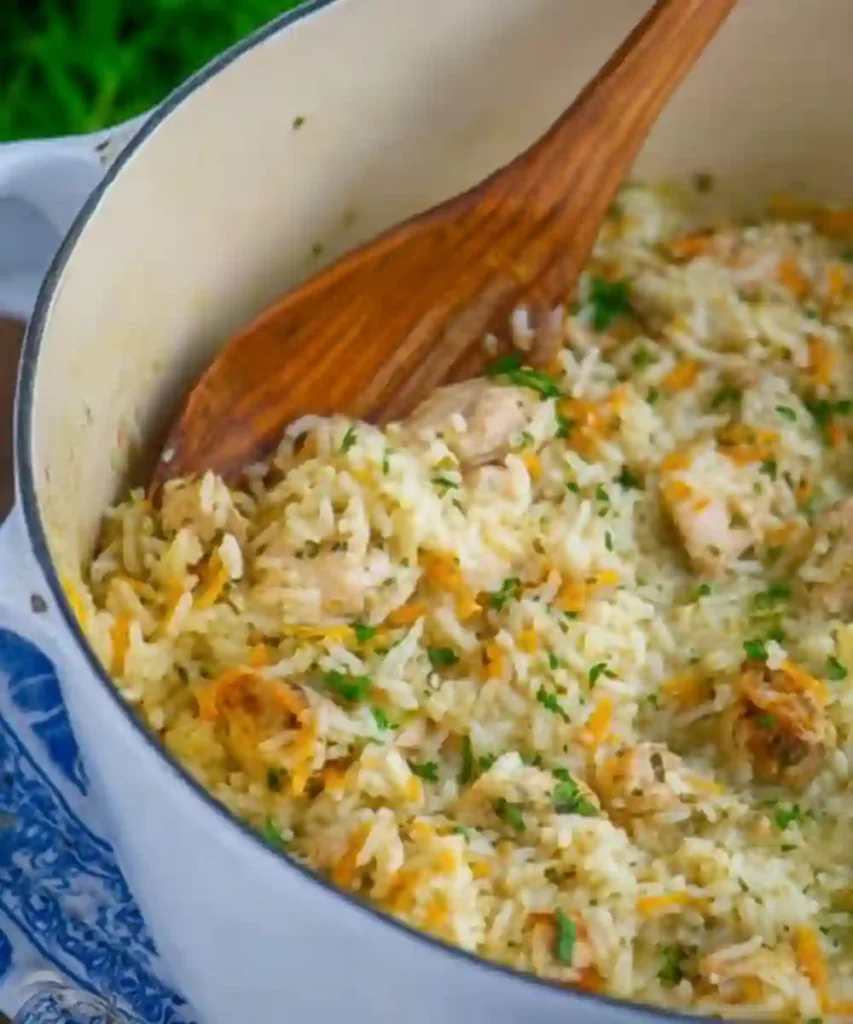 herbed chicken and rice cooked in white Dutch oven with grated carrot and wooden spoon