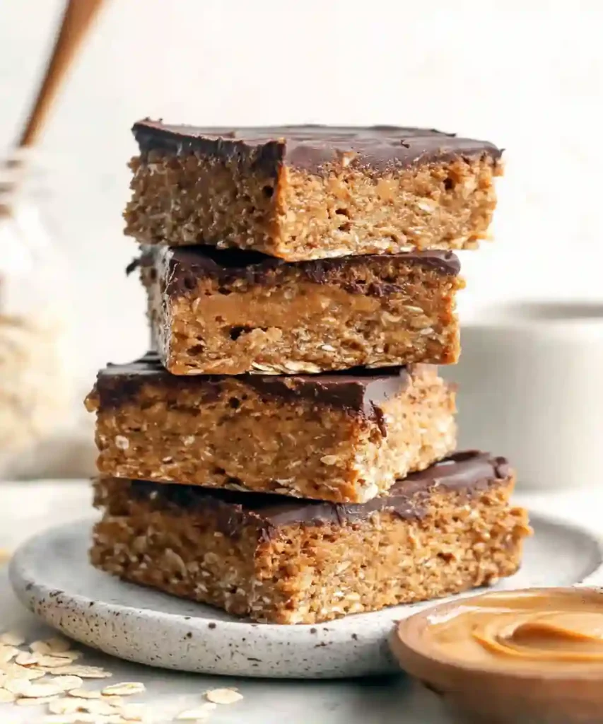 stack of peanut butter oat bars topped with dark chocolate on a ceramic plate