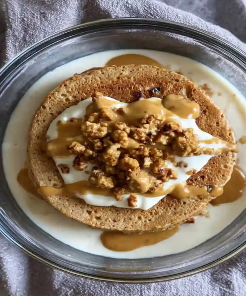 High-protein breakfast bowl with pancakes, Greek yogurt, granola, and peanut butter drizzle in glass dish