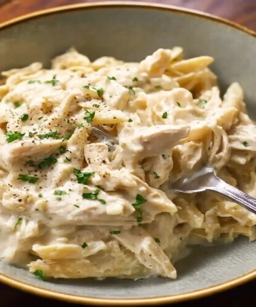 creamy slow cooker chicken alfredo pasta with parsley garnish in a bowl