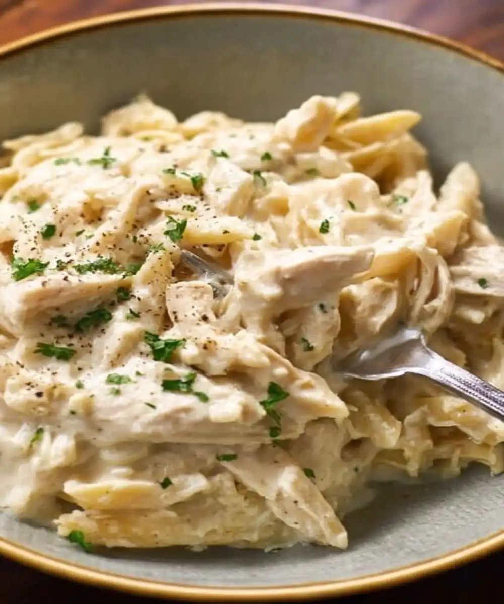 creamy slow cooker chicken alfredo pasta with parsley garnish in a bowl