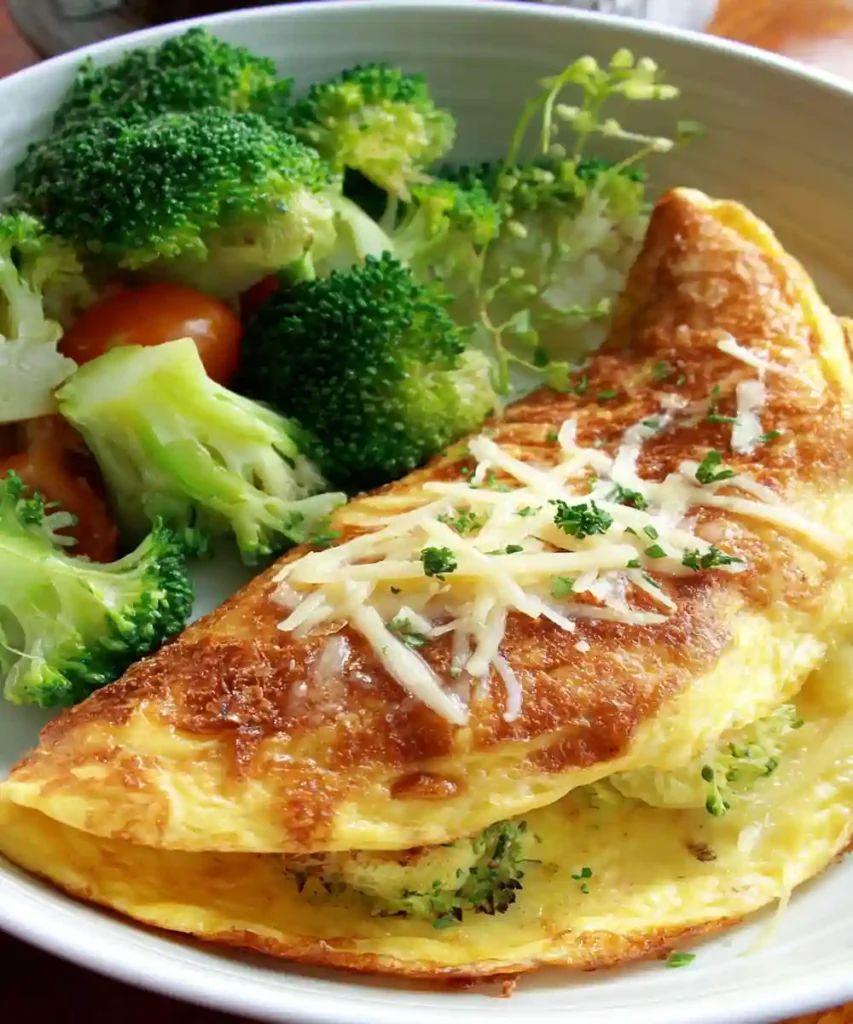 Golden omelette with shredded cheese and broccoli served with mixed vegetables in a white bowl