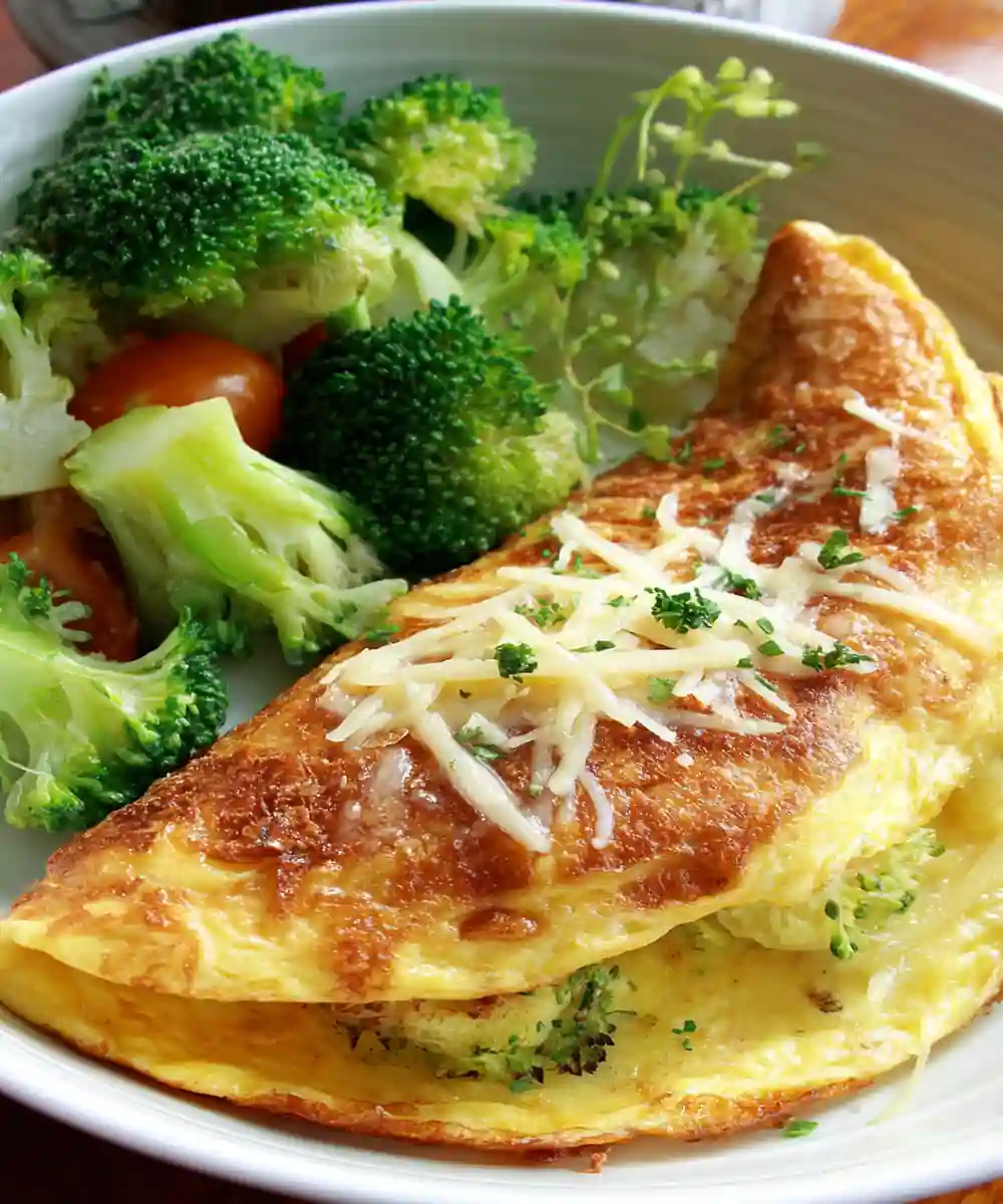Golden omelette with shredded cheese and broccoli served with mixed vegetables in a white bowl