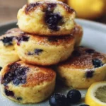 Blueberry lemon pancake bites stacked on a plate, topped with blueberries.