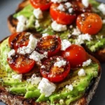 Avocado toast topped with crumbled feta cheese and cherry tomatoes on a plate