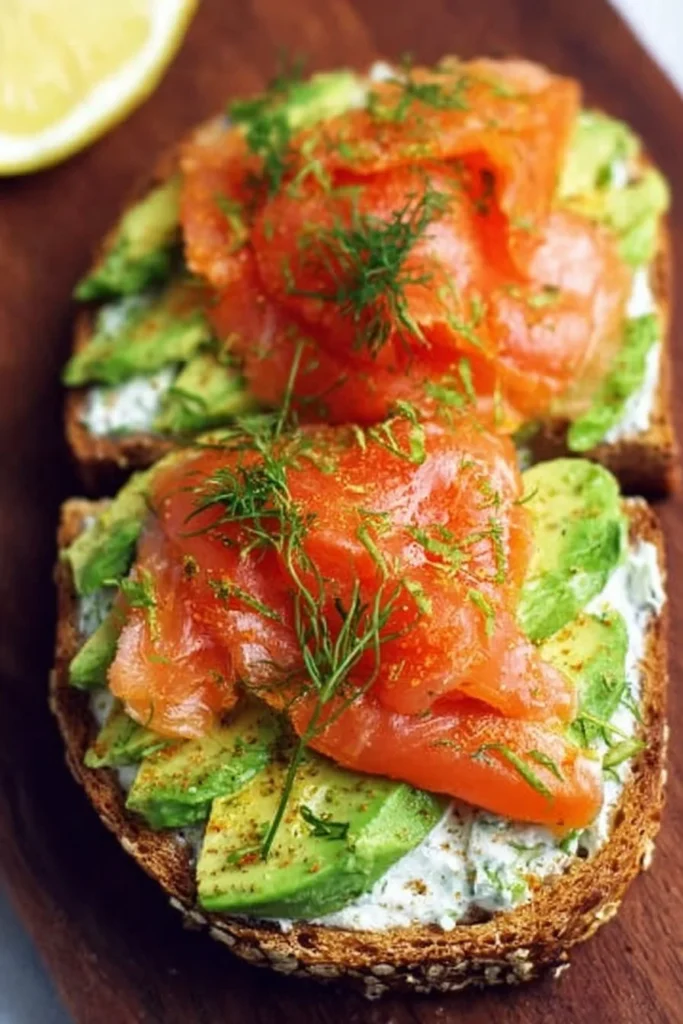 Avocado toast topped with smoked salmon and herbs on a rustic wooden table.