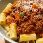 A bowl of Classic Bolognese Sauce served with pasta and fresh basil.