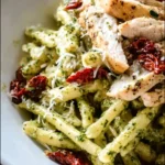 Creamy pesto pasta with chicken and sun-dried tomatoes in a bowl