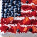 Patriotic Poke Cake topped with colorful frosting and berries for a festive look.
