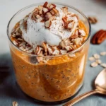 Bowl of quick pumpkin pie overnight oats topped with whipped cream and spices.