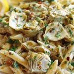 A bowl of Vegan Lemon Artichoke Pasta garnished with fresh herbs and lemon.